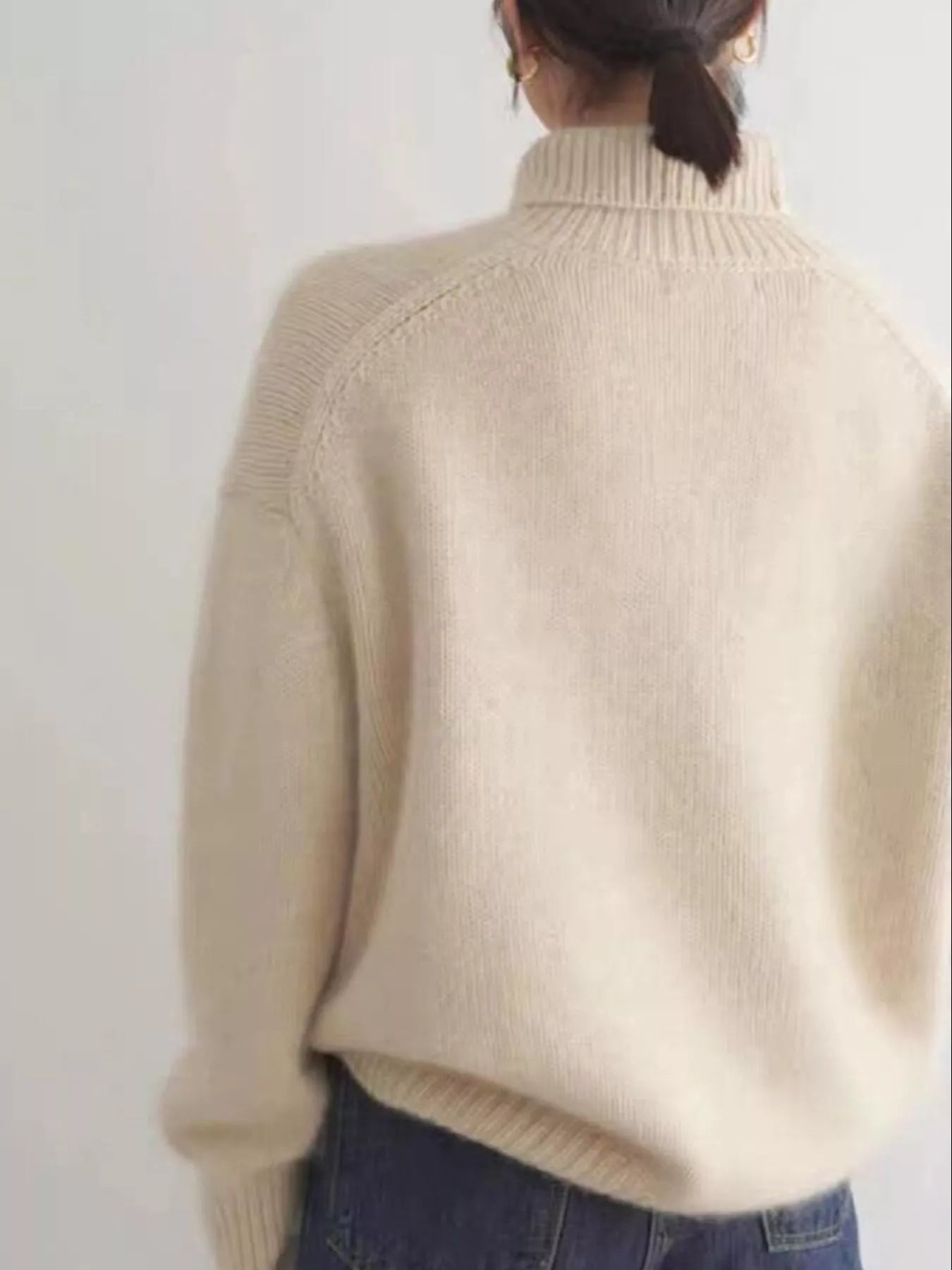 Person wearing a beige turtleneck sweater against a white background on NEWYORKLISTED.COM