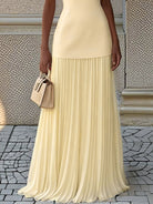 NEWYORKLISTED STYLE COLLECTION: Person wearing a beige pleated skirt and holding a matching handbag on a stone pavement.
