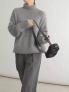 Person wearing a gray sweater and pants holding a black bag against a white background