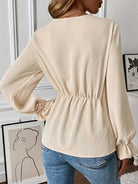 NEWYORKLISTED STYLE COLLECTION: Woman wearing a beige long-sleeve top with a subtle waistband, standing indoors.