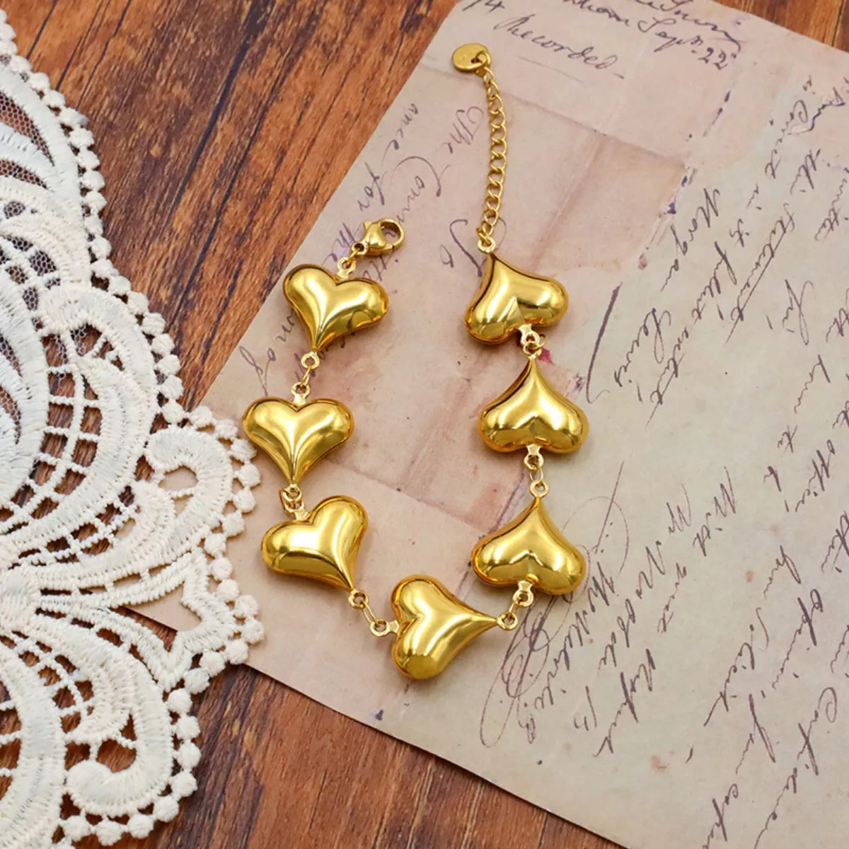 NYLD Glamour Collection by NEWYORKLISTED: Gold heart-shaped earrings on a wooden surface with lace and an old letter.