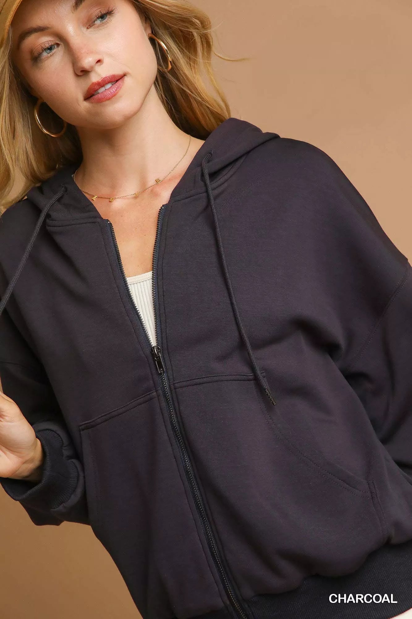 Woman wearing a charcoal gray hoodie against a beige background