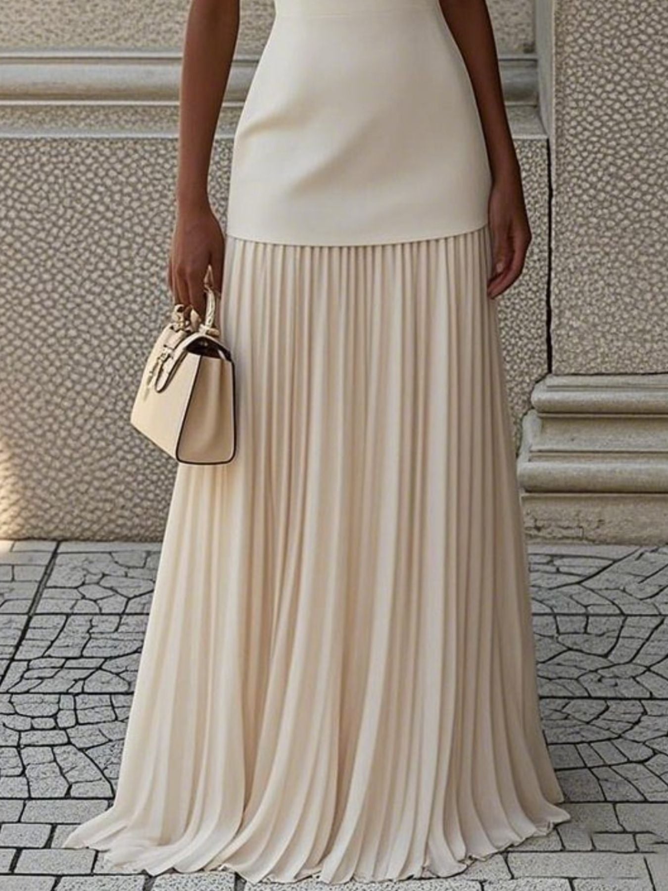 NEWYORKLISTED STYLE COLLECTION: Person wearing a beige pleated skirt and holding a matching handbag against a textured wall.