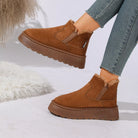 NEWYORKLISTED SHOE COLLECTION: A pair of women's brown suede ankle boots with a plush faux-fur lining and chunky platform soles, shown on a model wearing blue jeans against a white studio background with decorative faux fur.