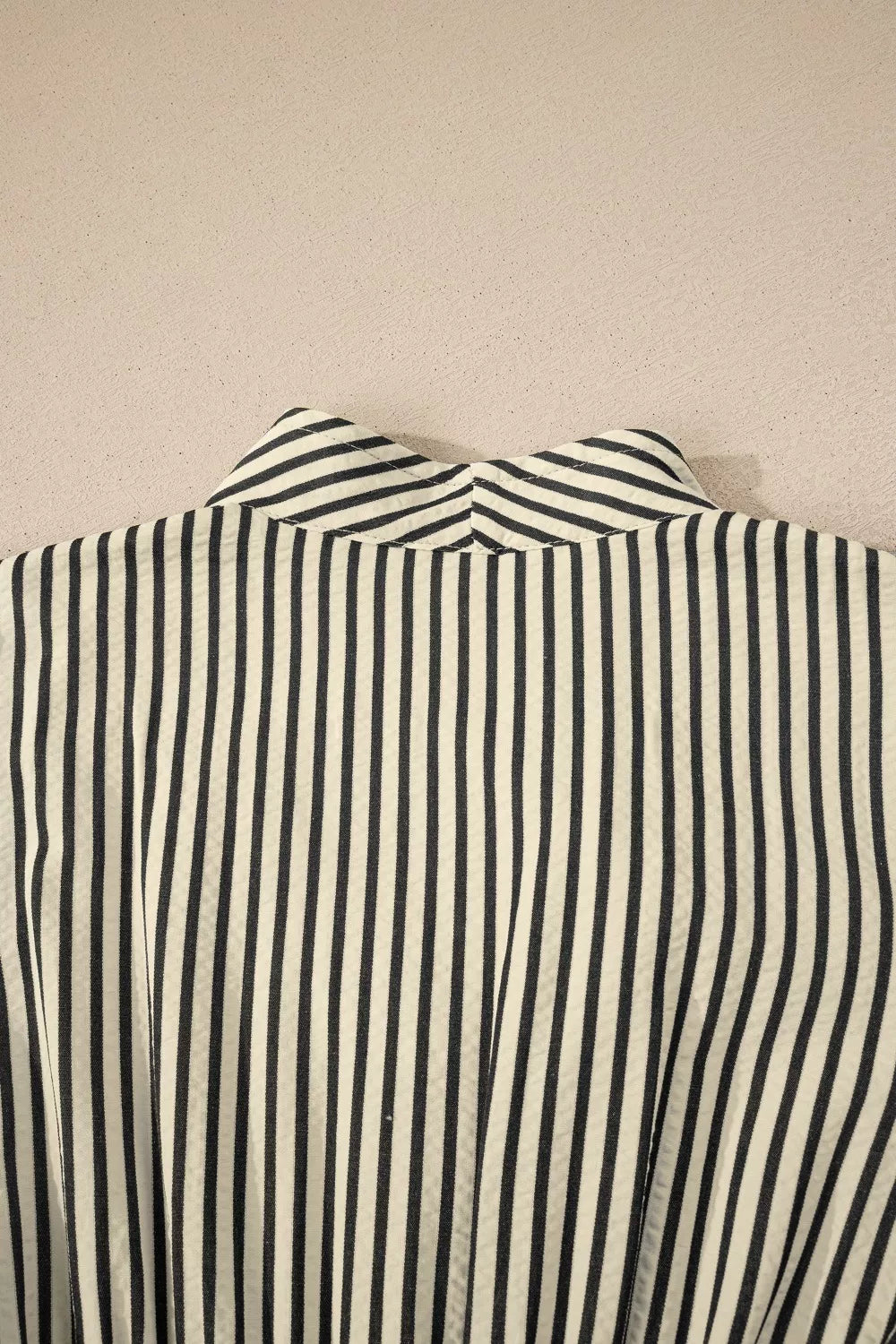 NEWYORKLISTED STYLE COLLECTION: Close-up of a black and white striped shirt collar on a beige background