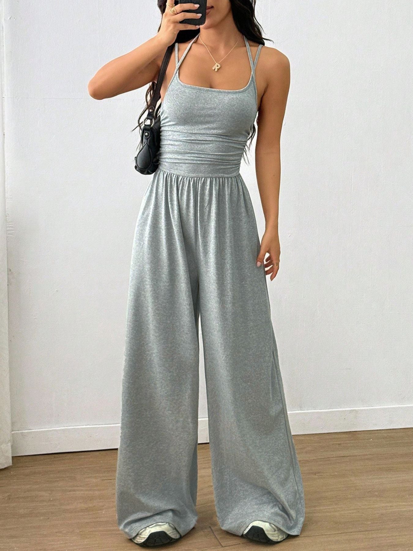 NEWYORKLISTED Comfort Collection: Woman wearing a gray jumpsuit against a white wall.
