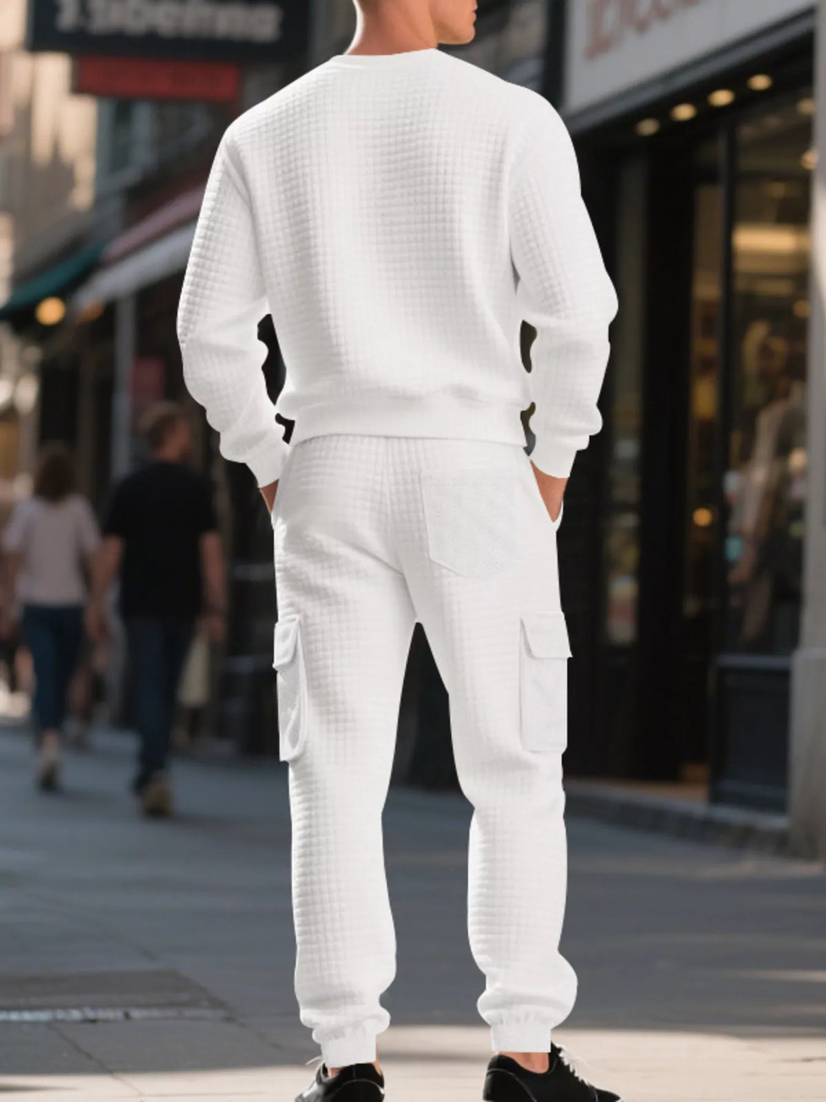 NEWYORKLISTED ATLAS MEN'S COLLECTION: A man standing on a city street, viewed from the back, wearing a matching white waffle-knit crewneck sweatshirt and cargo pants set.