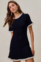 NEWYORKLISTED STYLE COLLECTION: Woman wearing a black dress with white trim on a plain background