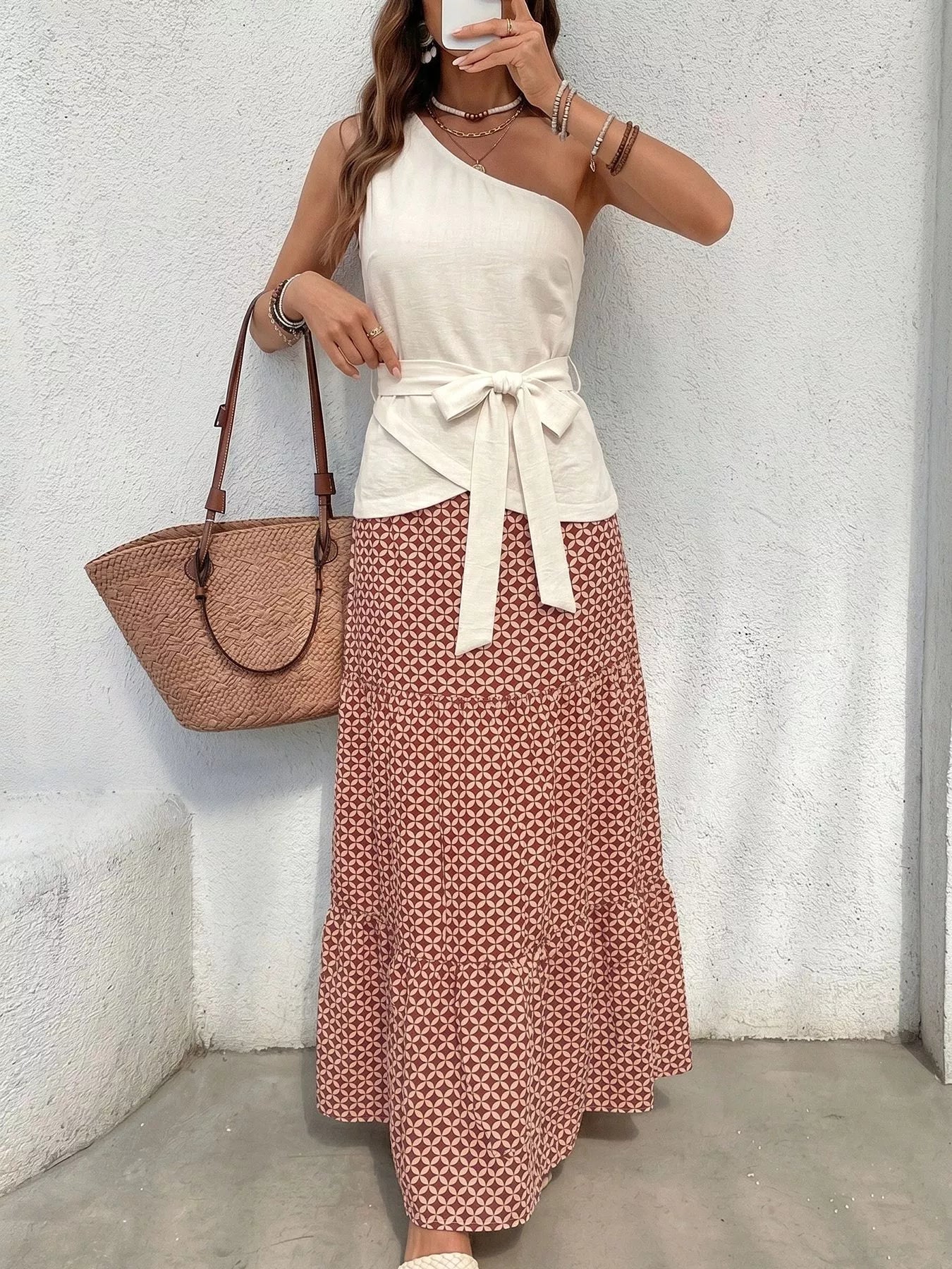 NEWYORKLISTED STYLE COLLECTION: Woman wearing a white top and patterned skirt with a brown bag against a light gray wall.