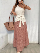 NEWYORKLISTED STYLE COLLECTION: Woman wearing a white top and patterned skirt with a brown bag against a light gray wall.