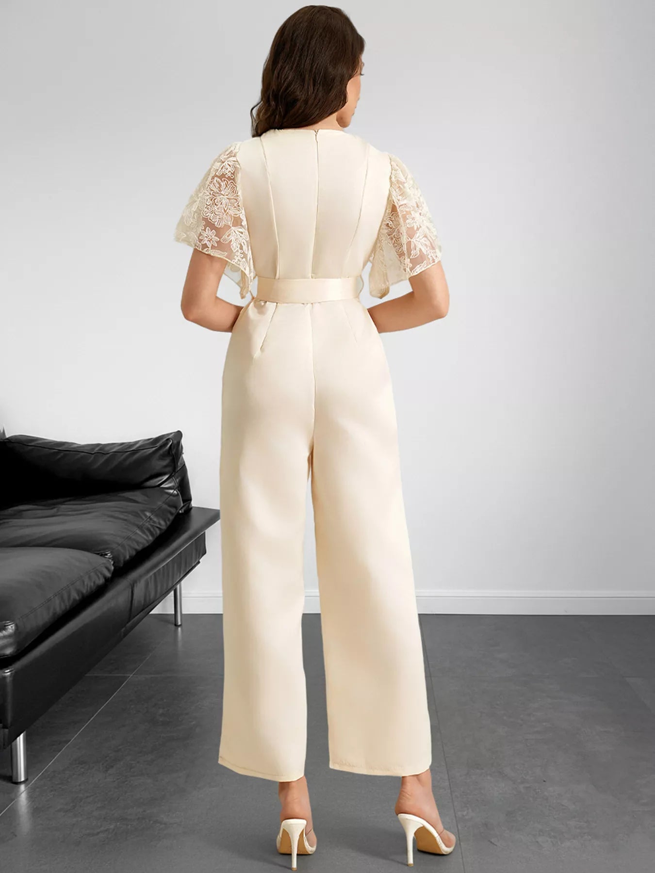NEWYORKLISTED STYLE COLLECTION: Woman wearing a beige jumpsuit with lace sleeves in a minimalistic room.