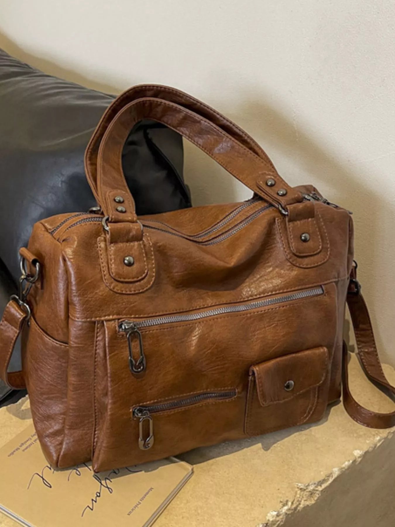 NEWYORKLISTED STYLE COLLECTION: Brown leather handbag on a cardboard surface with a neutral background