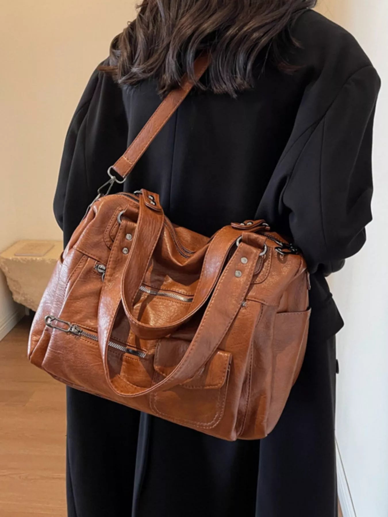 NEWYORKLISTED STYLE COLLECTION: Brown leather handbag held by a person wearing a black coat indoors.