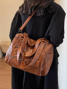 NEWYORKLISTED STYLE COLLECTION: Brown leather handbag held by a person wearing a black coat indoors.