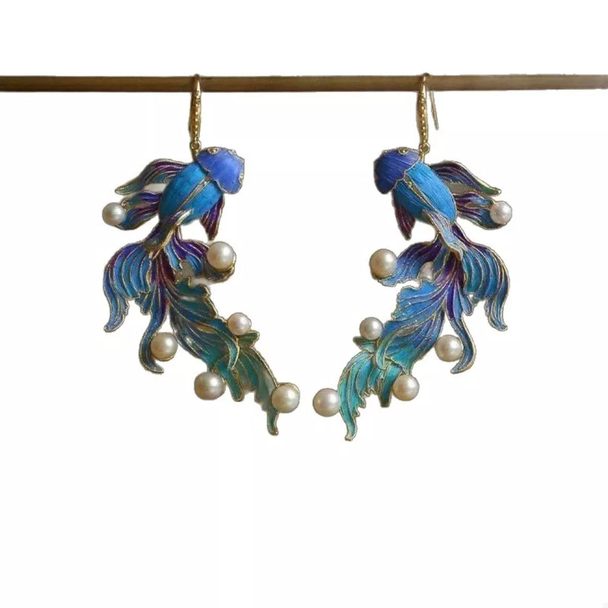 NYLD GLAMOUR By NEWYORKLISTED: Pair of fish-shaped earrings with enamel details and pearl accents on a white background