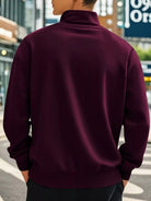 NEWYORKLISTED ATLAS MEN'S COLLECTION: Person wearing a maroon half-zip sweatshirt on a city street.