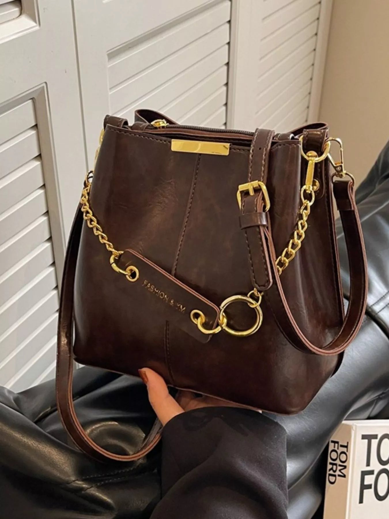 Brown handbag with gold accents held by a person against a neutral background New York Listed Style Collection 