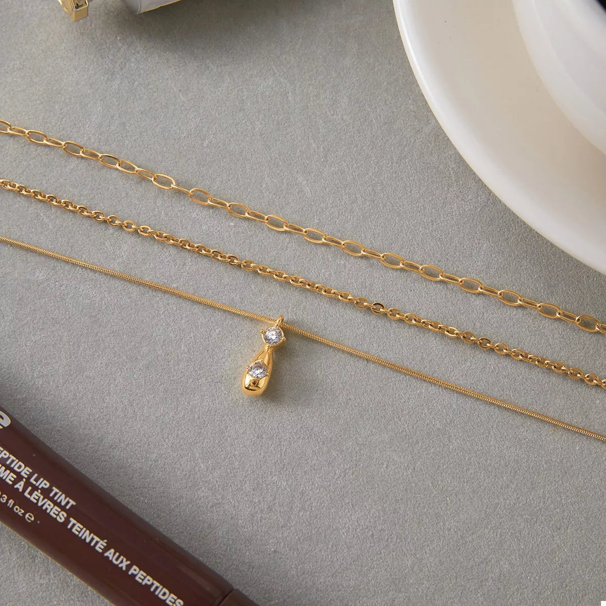 NYLD Glamour Collection by NEWYORKLISTED: Two gold necklaces on a gray surface with a white plate in the background.