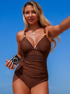 NEWYORKLISTED STYLE COLLECTION: Woman in a brown swimsuit holding a camera against a blue sky