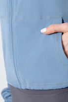 NEWYORKLISTED ACTIVEWEAR COLLECTION: Close-up of a person's hand touching the pocket of a light blue jacket against a white background