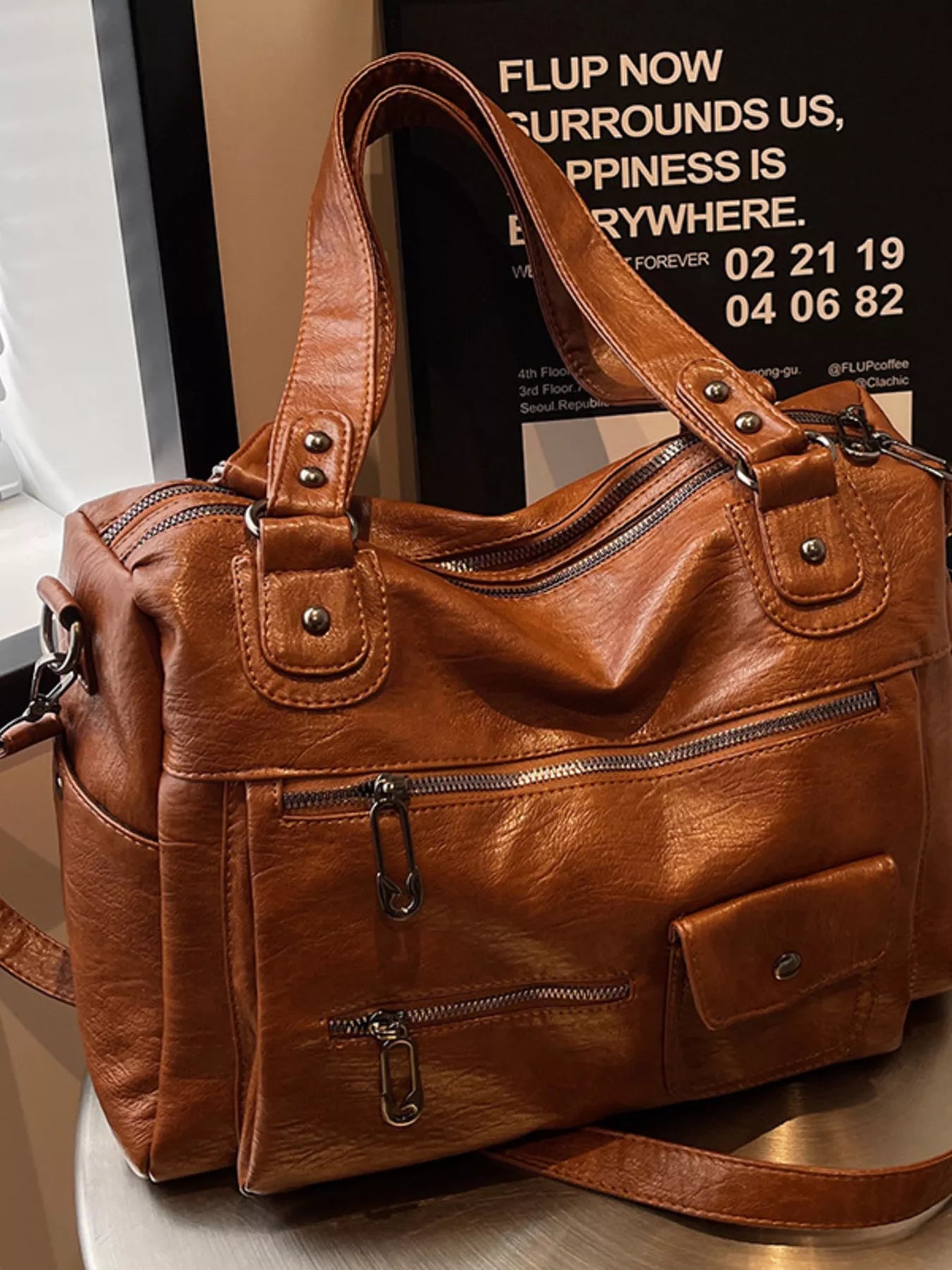 NEWYORKLISTED STYLE COLLECTION: Brown leather handbag on a surface with a blurred background