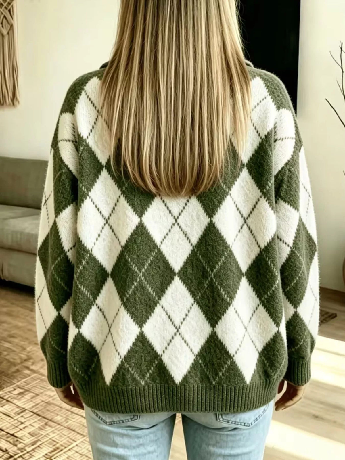 NEWYORKLISTED STYLE COLLECTION: A woman viewed from behind wearing an oversized knit sweater with an olive green and off-white argyle pattern, paired with light blue jeans in a home setting.