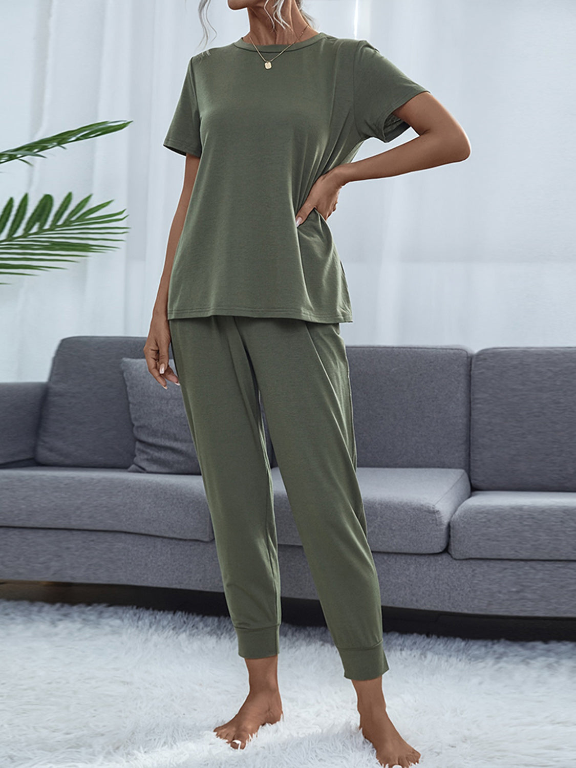 NEWYORKLISTED Intimate Apparel: Person wearing a green pajama set standing in front of a gray sofa.