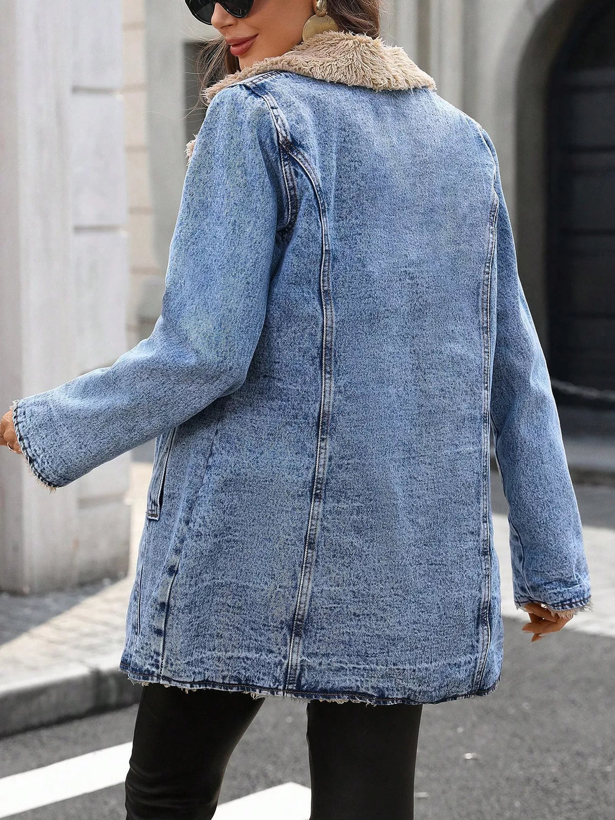 NEWYORKLISTED STYLE COLLECTION: A woman wearing a light blue denim jacket with a beige faux-fur collar, photographed from the back in an outdoor street setting.