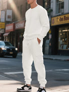 NEWYORKLISTED ATLAS MEN'S COLLECTION: A man wearing a matching white ribbed knit lounge set consisting of a long-sleeve crewneck sweater and jogger pants with cargo pockets, standing on a city street.