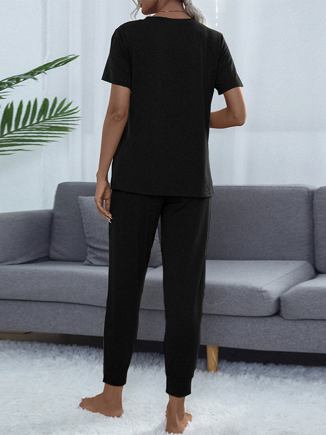 NEWYORKLISTED Intimate Apparel: Person wearing a black outfit standing in a living room with a gray sofa and white walls.