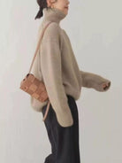 Person wearing a beige sweater holding a brown bag against a white background