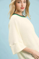NEWYORKLISTED STYLE COLLECTION: Woman wearing a light-colored ribbed sweater against a light blue background
