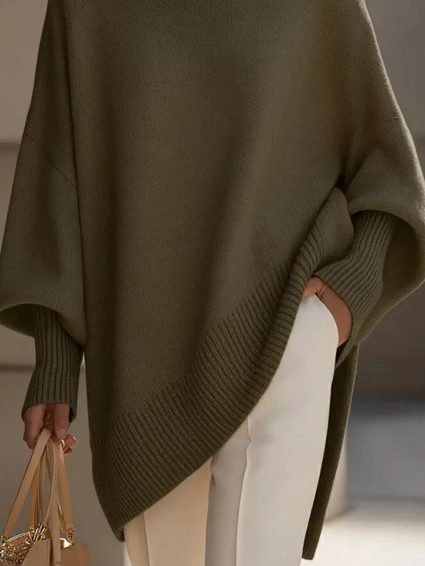 NEWYORKLISTED STYLE COLLECTION: Person wearing a green poncho holding a beige bag against a neutral background