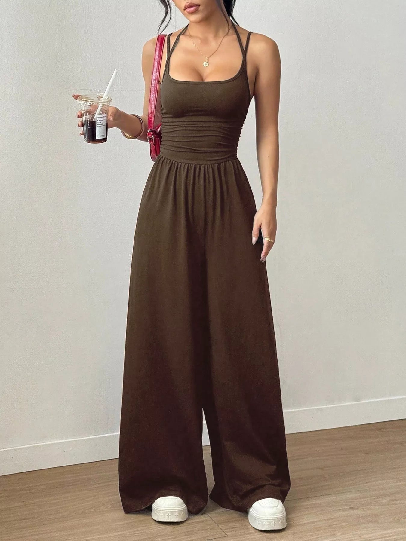 NEWYORKLISTED Comfort Collection: Woman wearing a brown jumpsuit holding a drink against a plain background