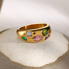 NYLD Glamour Collection by NEWYORKLISTED: Gold ring with colorful gemstones on a textured surface