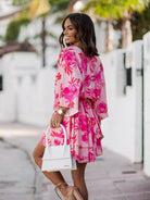NEWYORKLISTED STYLE COLLECTION: Woman wearing a pink floral dress holding a white handbag on a street.
