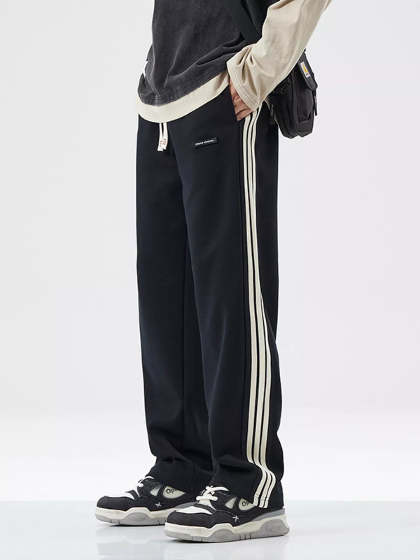 NEWYORKLISTED ATLAS MEN's COLLECTION: Black track pants with white stripes worn by a person on a white background