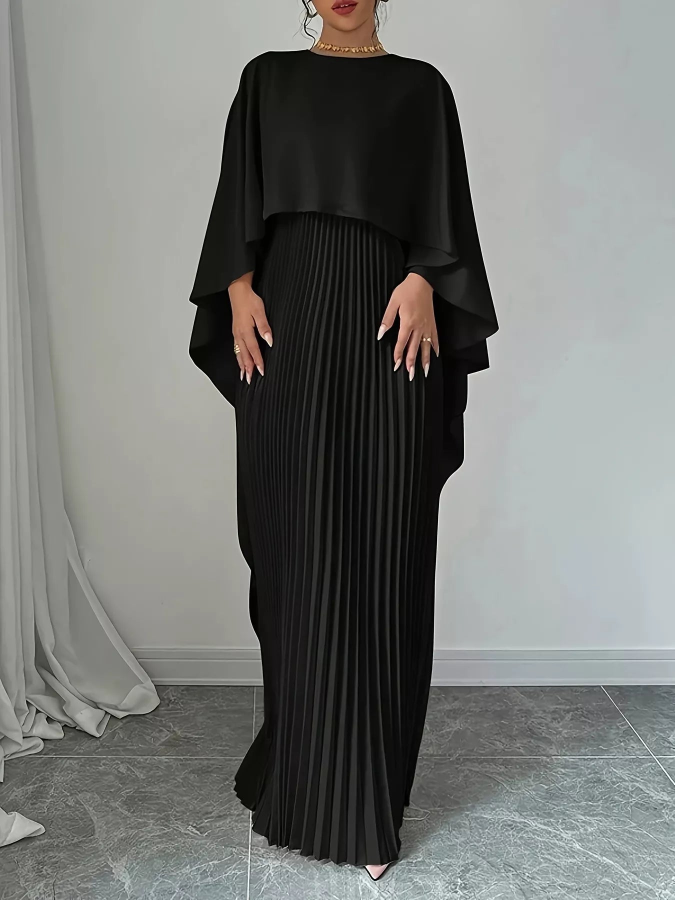NEWYORKLISTED STYLE COLLECTION: Woman wearing a black pleated dress with a draped top against a neutral background
