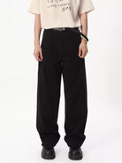 NEWYORKLISTED ATLAS MEN'S COLLECTION: A model wearing black wide-leg trousers with a black belt, paired with a cream graphic t-shirt and black shoes, photographed against a solid white studio background.