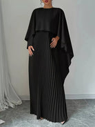 NEWYORKLISTED STYLE COLLECTION: Woman wearing a black pleated dress with a cape-like top against a neutral background