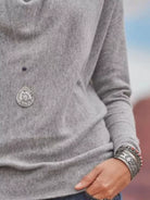 NEWYORKLISTED STYLE COLLECTION: Gray sweater with a decorative button and silver bracelet on a blurred background