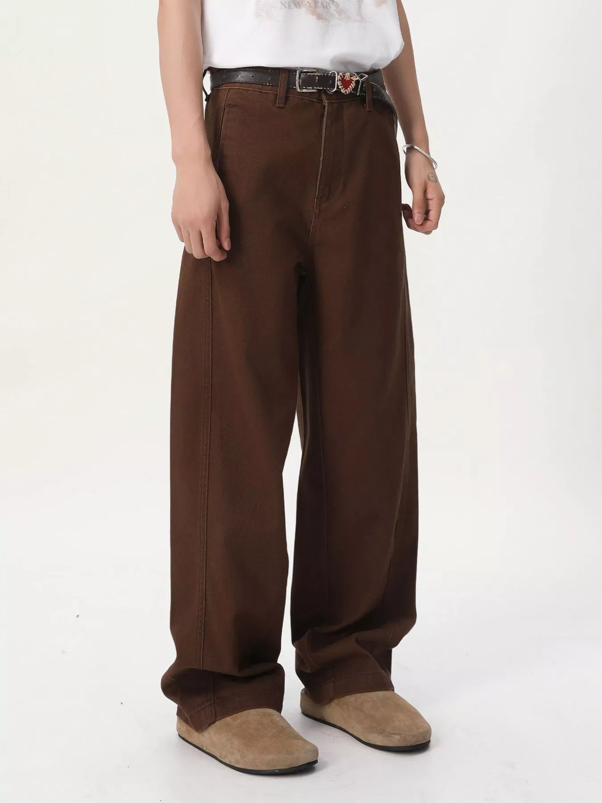 NEWYORKLISTED ATLAS MEN'S COLLECTION: A person wearing loose, wide-leg brown pants with a black belt, a white top, and tan slip-on shoes, photographed against a plain light background.