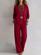 NEWYORKLISTED STYLE COLLECTION: A woman modeling a matching deep red long-sleeve top and wide-leg pants set, accessorized with layered silver necklaces, bracelets, and sandals, against a plain light gray background.