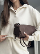 NEWYORKLISTED Comfort Collection: Person holding a brown handbag with a neutral background