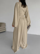 NEWYORKLISTED STYLE COLLECTION: Person wearing a beige jumpsuit in a minimalistic room.