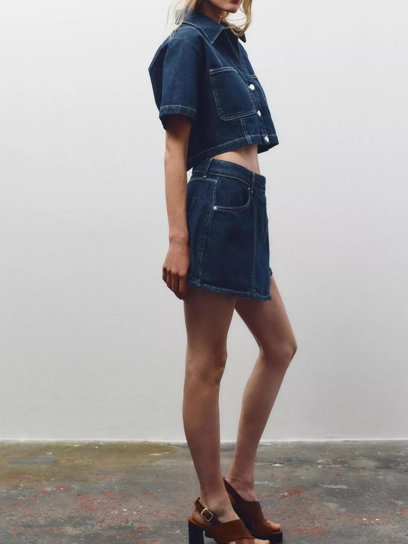 NEWYORKLISTED STYLE COLLECTION: Person wearing a denim outfit with a skirt and jacket against a plain background