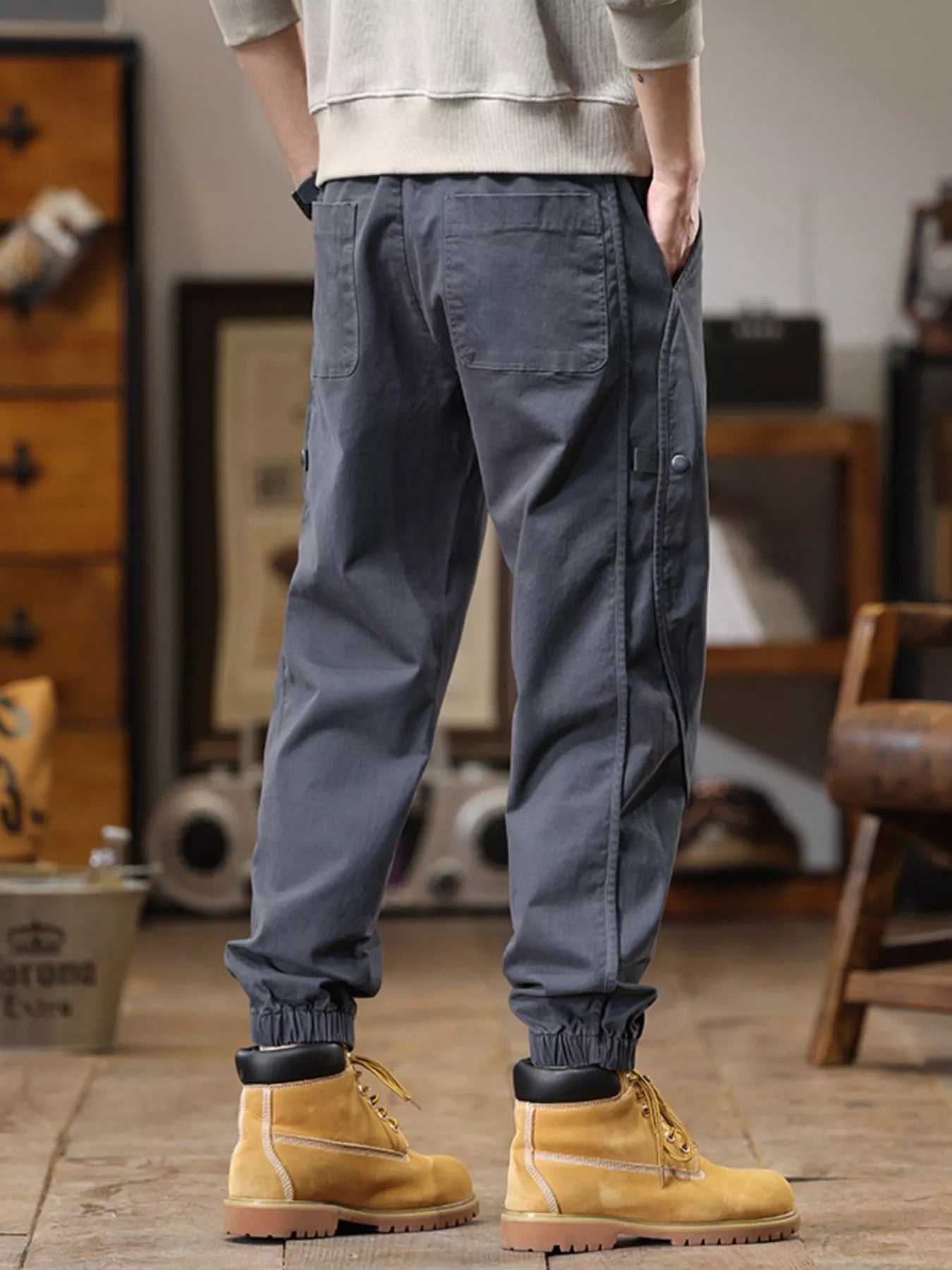 NEWYORKLISTED ATLAS MEN'S COLLECTION: Person wearing gray cargo pants and yellow boots in a room with wooden furniture.