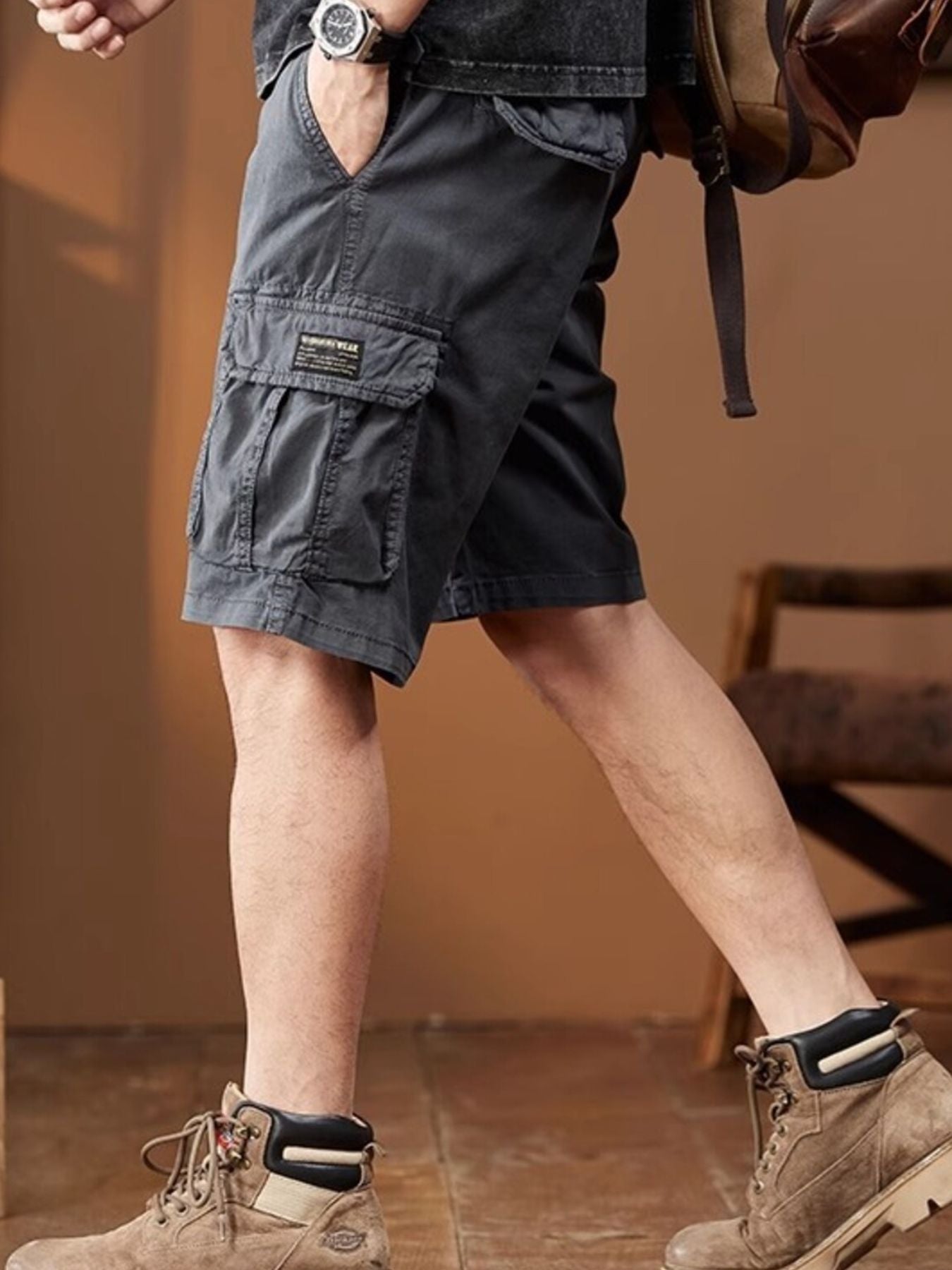 NEWYORKLISTED ATLAS MEN's COLLECTION: Person wearing gray cargo shorts with a brown backpack indoors.