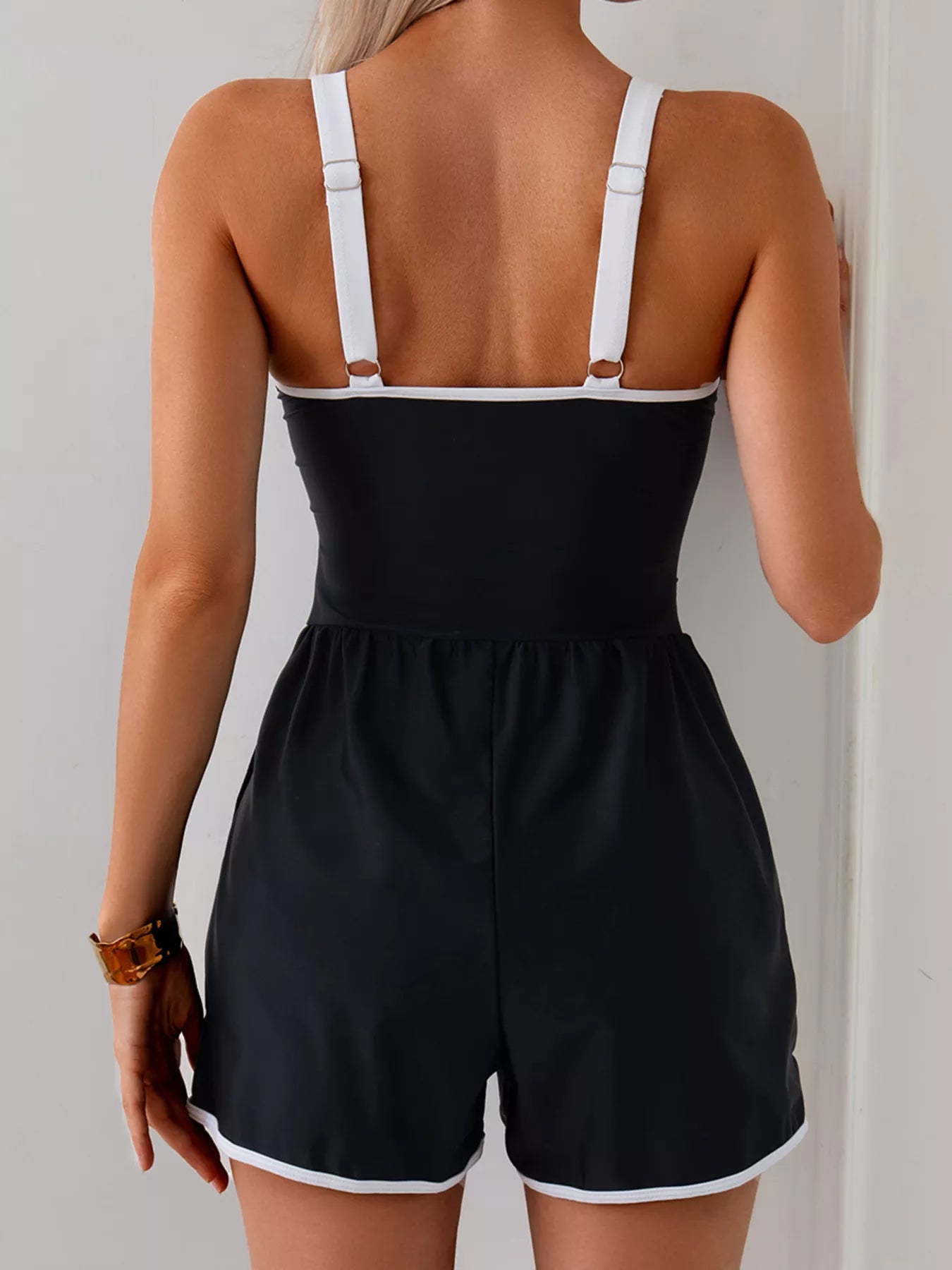 NEWYORKLISTED STYLE COLLECTION: Black romper with white straps worn by a person on a plain background