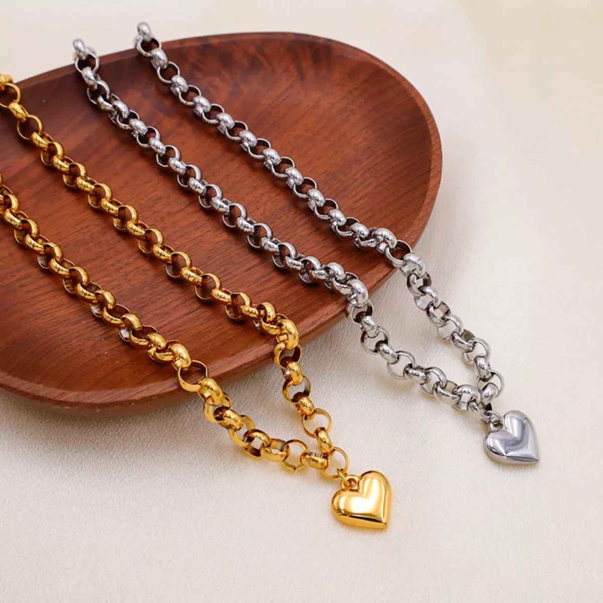 NYLD Glamour Collection by NEWYORKLISTED: Three gold and silver chain necklaces with heart pendants on a wooden plate.